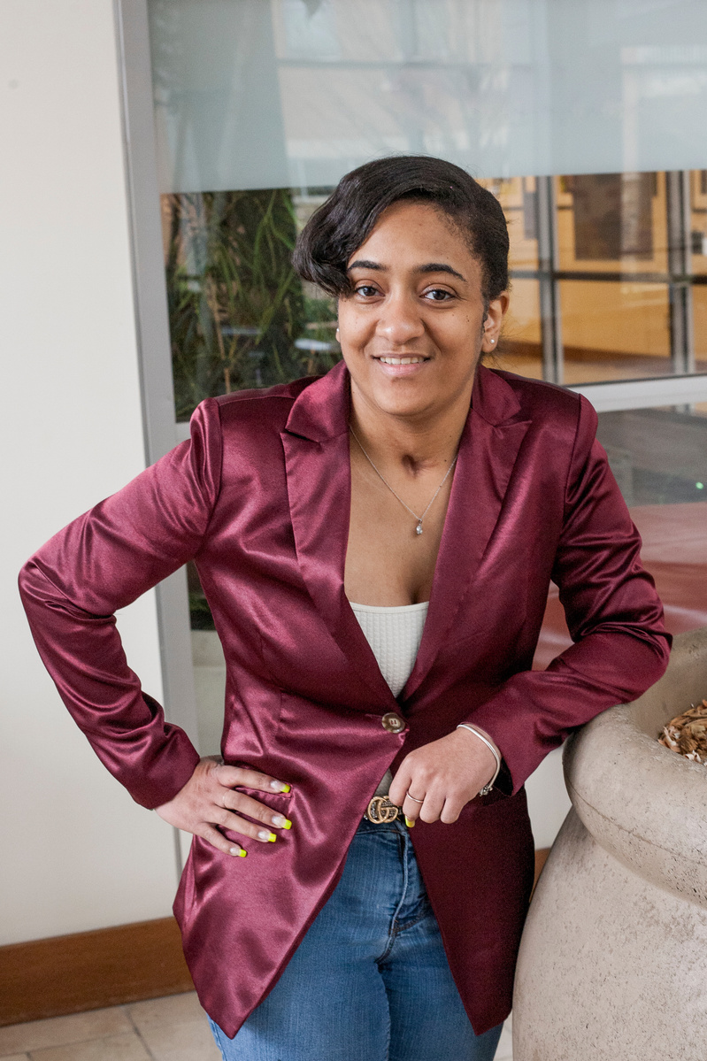 Tavia is an African American college student wearing a rose blazer and jeans. 