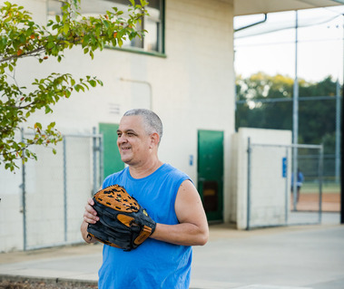A man wears a blue sleeveless shirt and has a baseball glove on his hands. 