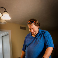A man stands in a blue polo shirt and looks at a book on a table. 