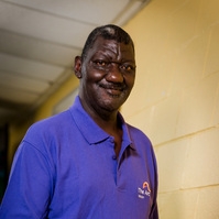 A middle aged African American man wears a purple polo shirt and paints a wall cream.