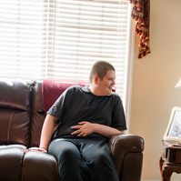 A white teenaged boy laughs as he sits on a sofa. 