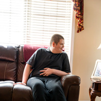 A white teenaged boy laughs as he sits on a sofa. 