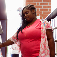 A young African American woman looks at books on shelves in a library.