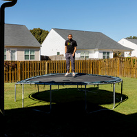 Young man stands on trampoline in a yard on a sunny day.