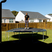Young man stands on trampoline in a yard on a sunny day.