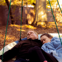 A father and daughter lay in a disc swing outside.