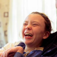 A young girl wearing a blue shirt laughs at the camera.