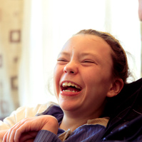 A young girl wearing a blue shirt laughs at the camera.