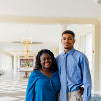 Two students wear blue shirts and stand in a bright hallway. 