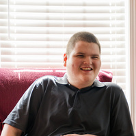A white teenaged boy laughs as he sits on a sofa. 
