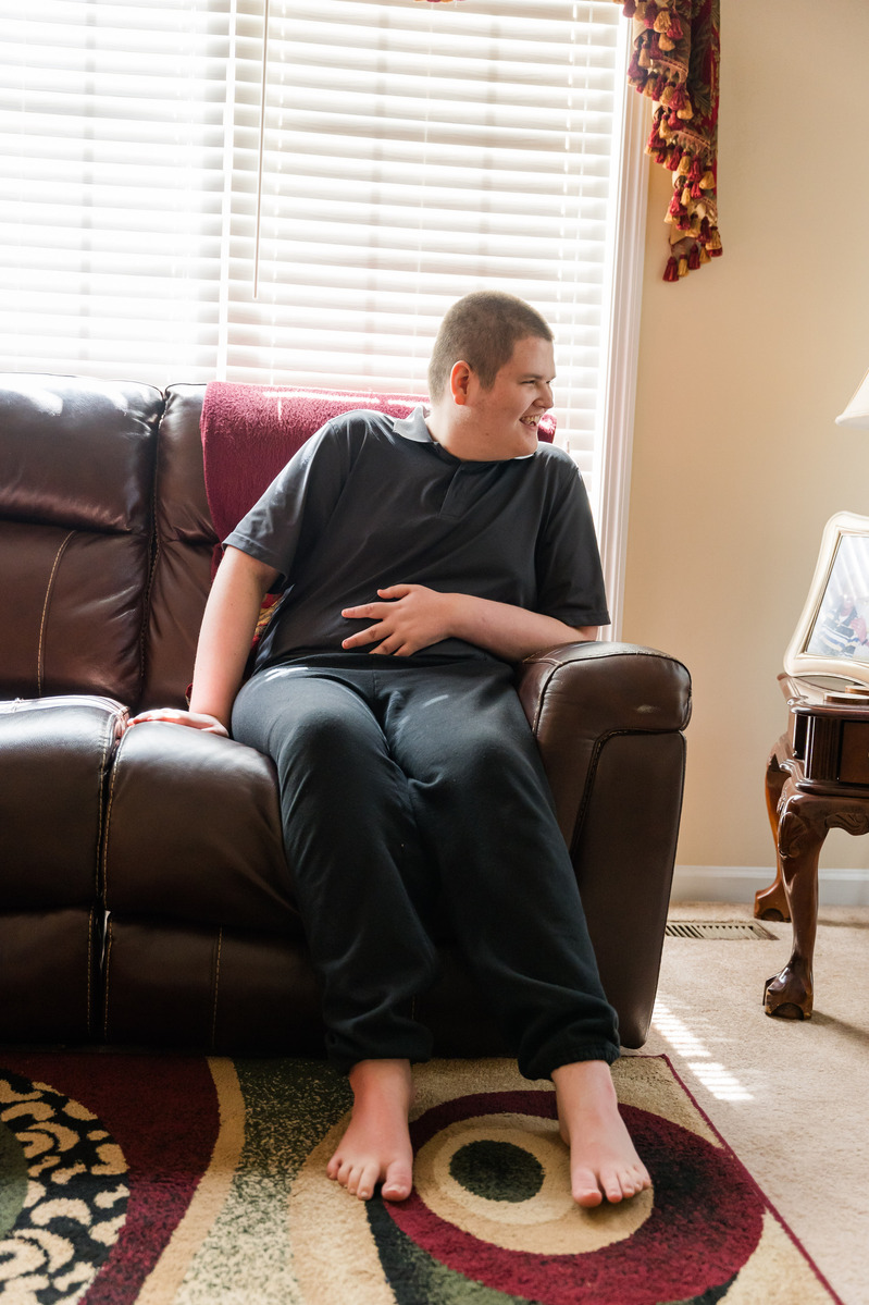A white teenaged boy laughs as he sits on a sofa. 