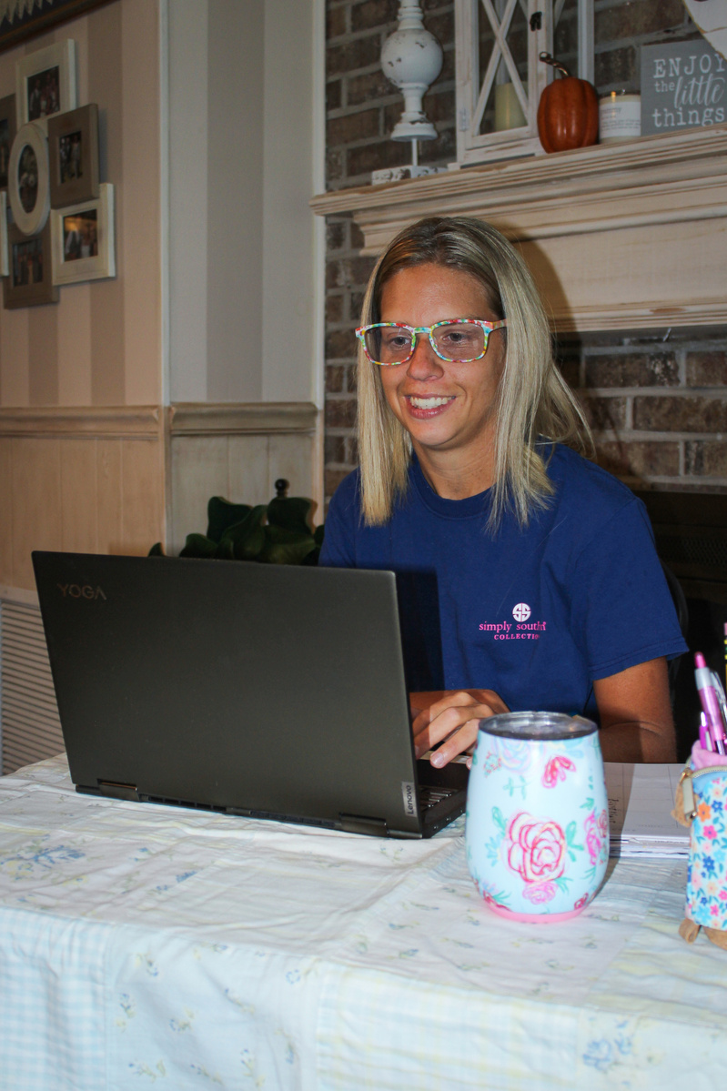 A blond woman wears glasses and sits in front of a laptop computer.  