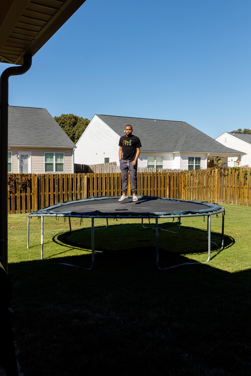 Young man stands on trampoline in a yard on a sunny day.