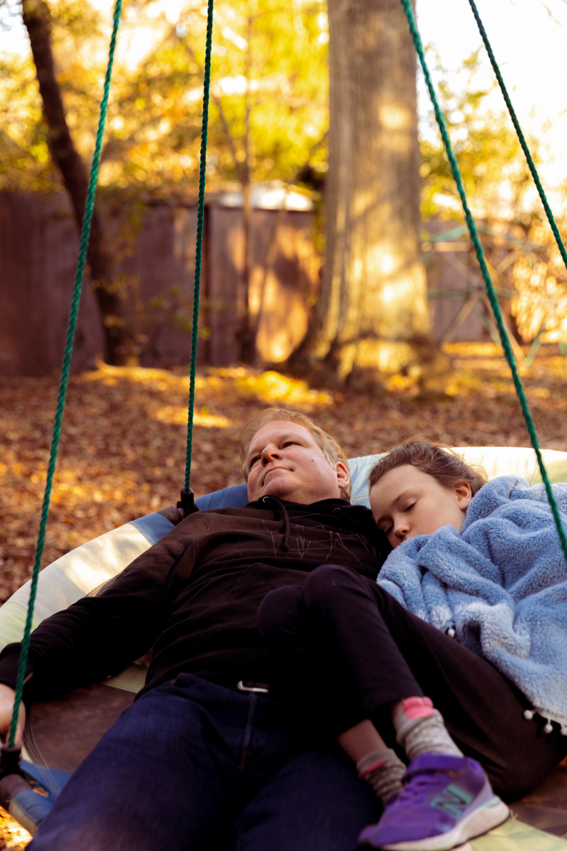A father and daughter lay in a disc swing outside.