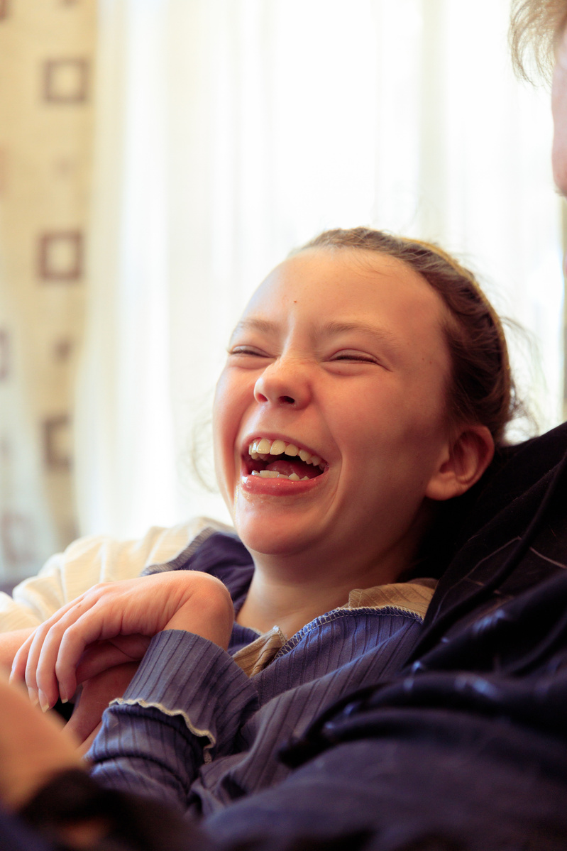 A young girl wearing a blue shirt laughs at the camera.