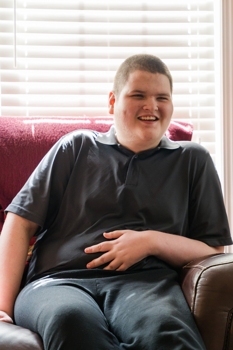A white teenaged boy laughs as he sits on a sofa. 