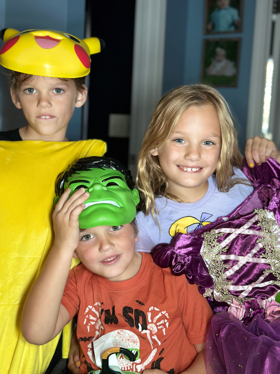 Three children in costumes smile for the camera. 
