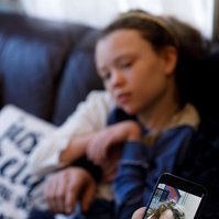 A phone shows a photo of a toddler making a goofy face. The same girl, now 11, sits behind the phone. 
