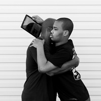 A black and white image of a young man and his father hugging. 