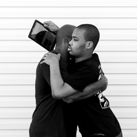 A black and white image of a young man and his father hugging. 