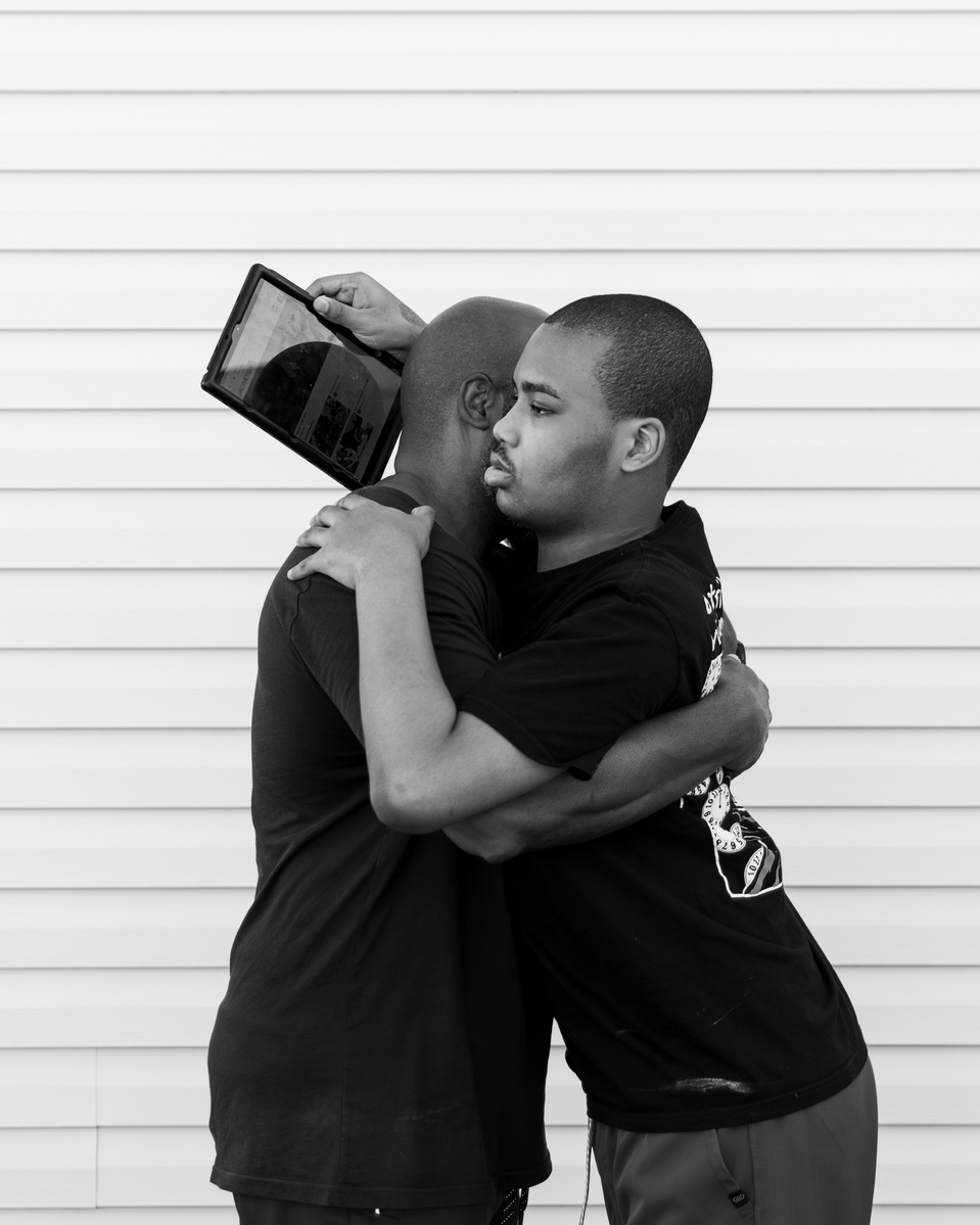 A black and white image of a young man and his father hugging. 