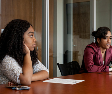 Two African American female college students, Skye and Tavia, sit at a conference table.
