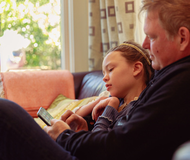Man cuddles with young daughter on a sofa. 