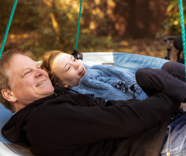 Father and daughter lay on a disc swing outside. 