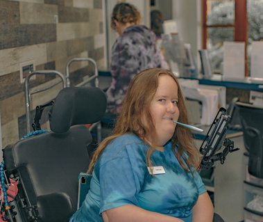 Woman with red hair wears a blue t-shirt and uses a stylus to type on her phone. 