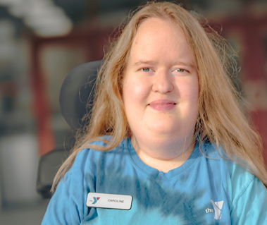 Woman with red hair wears a blue t-shirt and a name tag that reads Caroline. 