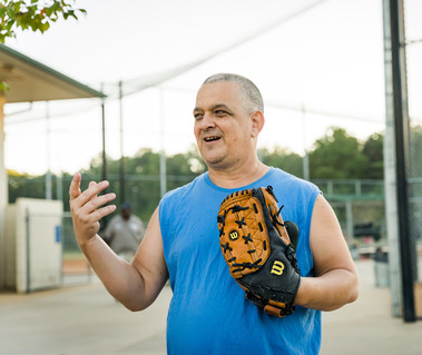 A man wears a blue sleeveless shirt and has a baseball glove on his hands. 