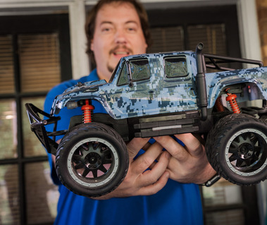 A man in a blue polo shirt holds a remote-controlled truck. 