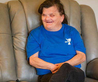 Brunette woman wears a blue t-shirt and sits in a leather chair. 