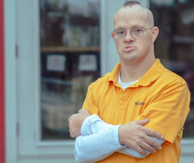 Man wears glasses and a yellow polo shirt with his hands folded across his chest.