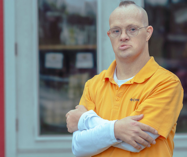 Man wears glasses and a yellow polo shirt with his hands folded across his chest.