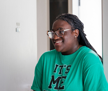 A young African American woman with her hair in braids wears glasses and a green shirt. 