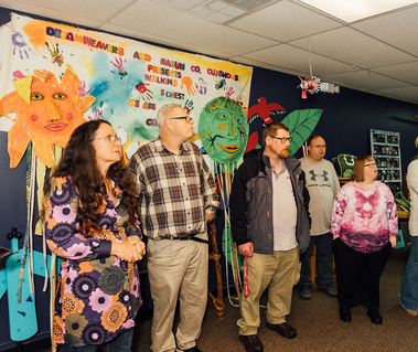 A group of people stand in front of a large mural and talk.