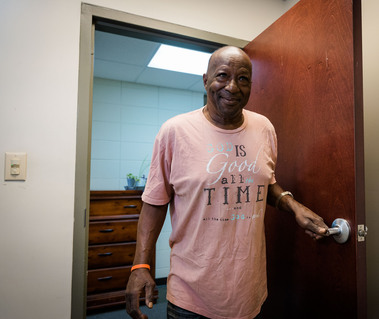 A man stands in the doorway wearing a pink shirt.