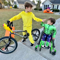 Tow boys wear Halloween costumes and high five each other on the sidewalk. 