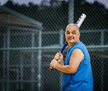 A man wears a blue sleeveless shirt and swings a baseball bat.