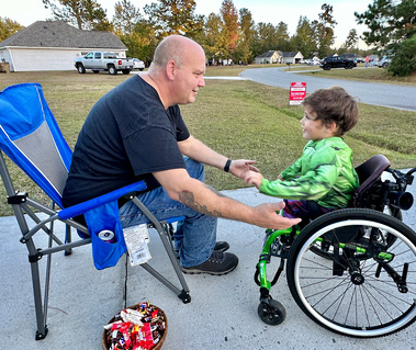 A young boy in a Hulk costume sits in a wheelchair and smiles at an older man who is seated across from him. 