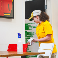 A young woman in a yellow hat and t-shirt clears a restaurant table. 