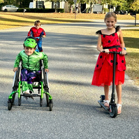 Three children in Halloween costumes go down a street. 