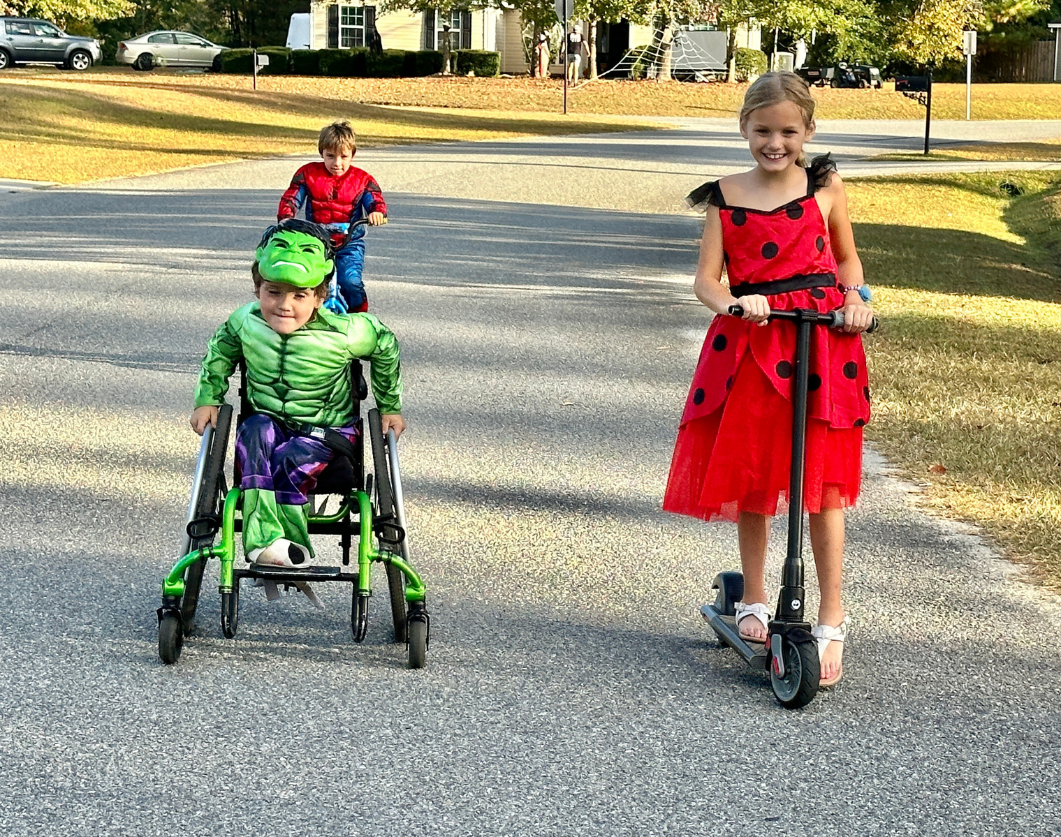 Three children in Halloween costumes go down a street. 
