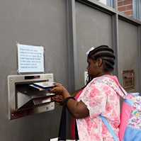 A young African American woman with braids in her hair and a pink flowered shirt puts books into a library return bin.