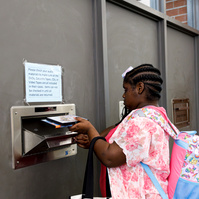 A young African American woman with braids in her hair and a pink flowered shirt puts books into a library return bin.