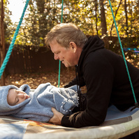 A father lays his daughter in a disc swing on a sunny day. 