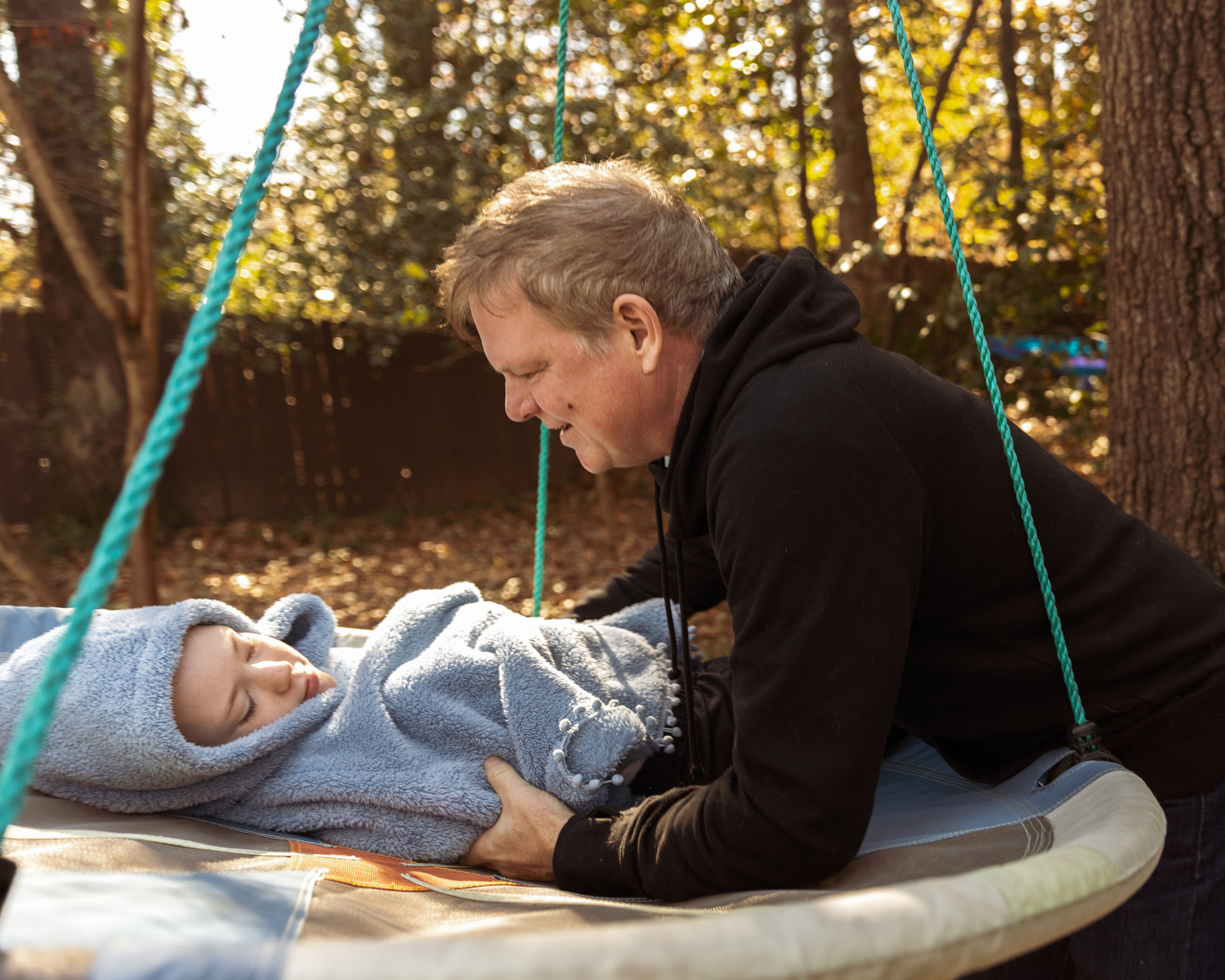 A father lays his daughter in a disc swing on a sunny day. 