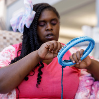 A young African American woman uses a circle loom with yarn.