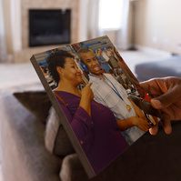 The hands of an African American man hold a photo of a woman and a young man. 